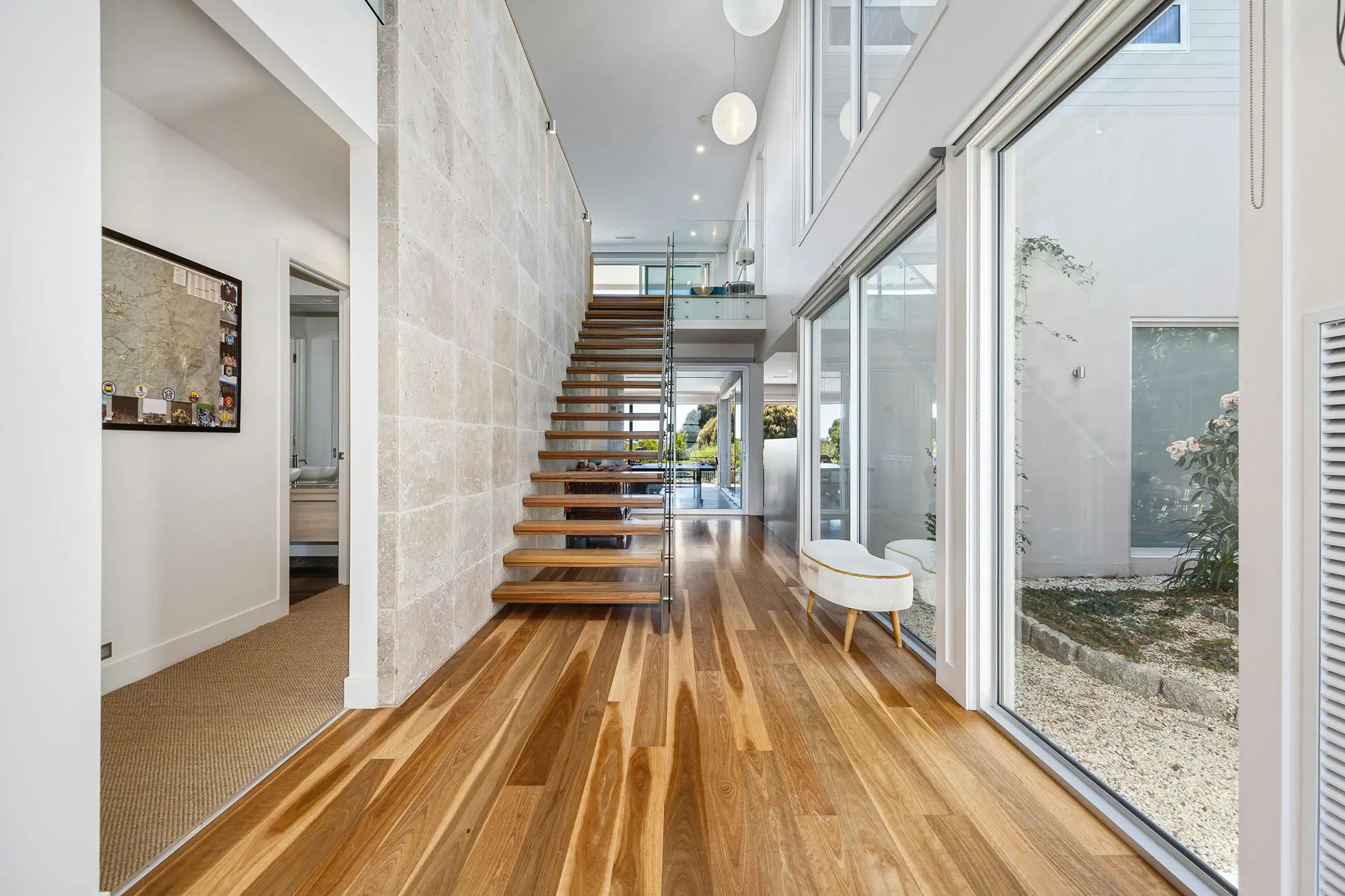 Spacious modern hallway with wooden floors, an open staircase, and floor-to-ceiling windows. Bright, airy atmosphere with natural light.