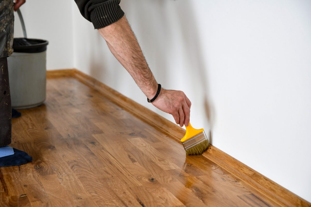 Lacquering wood floors. Worker uses a brush to coating floors. Varnishing lacquering parquet floor by paintbrush - second layer. Home renovation parquet